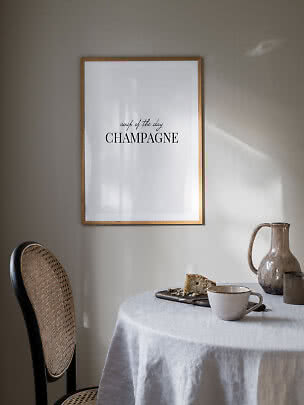 Plakat i træramme med teksten "soup of the day CHAMPAGNE" over et dækket bord.