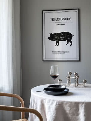 Gerahmtes schwarz-weiß Poster mit Schweinefleisch-Zuschnitten über gedecktem Tisch an grauer Wand
