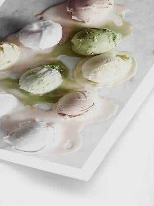Plusieurs boules de glace fondantes vert pâle, blanches et roses sur une plaque blanche