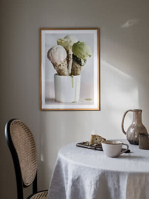 Poster incorniciato con tre coni gelato in una tazza bianca su una parete beige sopra un tavolo.
