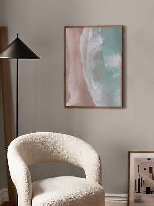Framed beach wave print on wall above a cream boucle chair beside a black floor lamp