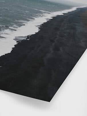 Luftfoto af bølger langs en sort sandstrand