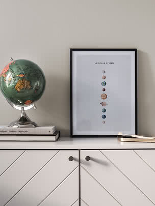 Affiche encadrée du système solaire sur un meuble blanc, à côté d’un globe sur des livres