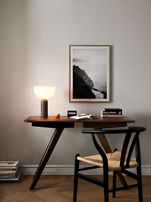 Dark wooden desk with chair, lit table lamp and framed black-and-white landscape photo
