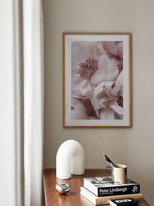 Lámina floral en rosa suave enmarcada sobre una mesa de madera con libros, taza y adorno blanco.