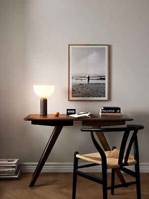 Scrivania in legno scuro con lampada accesa, sedia e foto in bianco e nero della spiaggia incorniciata