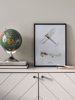 Inramad poster med vintage flygplansritningar på vit byrå bredvid en jordglob