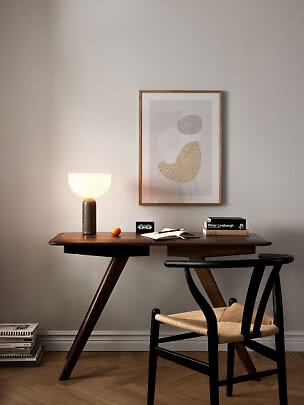 Scrivania in legno scuro con lampada da tavolo accesa, sedia e stampa astratta al muro.
