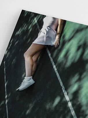 Mujer con vestido blanco y zapatillas blancas recostada en pista oscura con líneas blancas