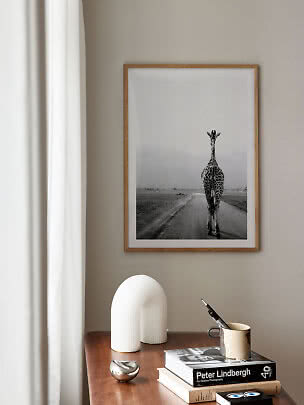 Inramad svartvit giraffbild över ett träbord med böcker och dekorationer