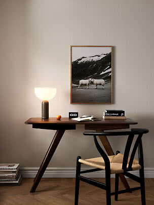 Houten bureau met zwarte stoel, tafellamp en ingelijste foto aan beige muur