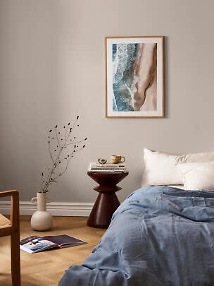 Dormitorio con ropa de cama azul, cojines blancos y cuadro de playa en pared beige