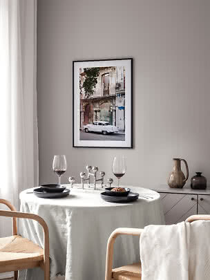 Framed photo art of a white vintage car by a weathered building above a set dining table