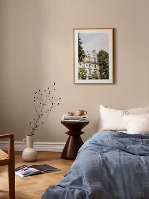 Gemütliches Schlafzimmer mit blauer Bettdecke, Beistelltisch, Vase und gerahmtem Stadtfoto an beiger Wand