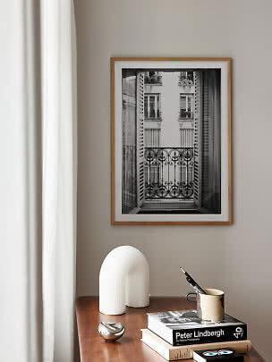 Framed black-and-white balcony photo on beige wall above wooden table with books and vase