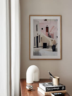Framed photo print of pastel buildings above a wooden table with books and decor