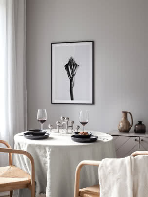 Esstisch mit weißer Tischdecke, schwarzen Tellern, Weingläsern und schwarz-weißem Blumenbild