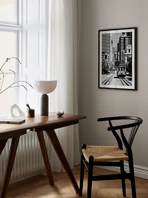 Stampa urbana in bianco e nero con cornice nera sopra una scrivania in legno in una stanza luminosa.