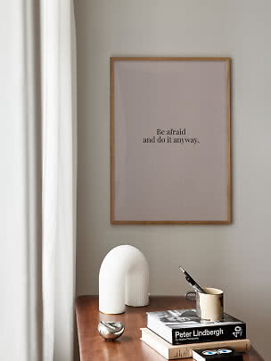 Plakat w drewnianej ramie z napisem "Be afraid and do it anyway" nad stołem z książkami