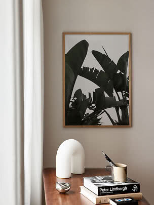 Indrammet botanisk plakat med mørke blade over et træbord med bøger, kop og hvid lampe