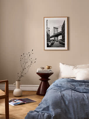 Bedroom with blue duvet, dark side table and framed black-and-white bridge print on beige wall
