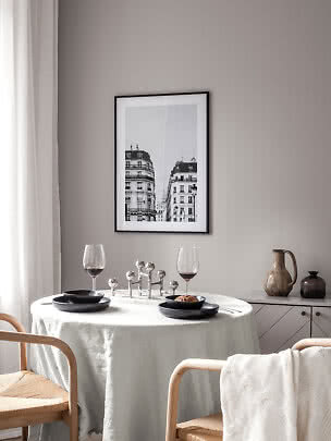 Rincón de comedor con mesa redonda, platos negros, copas de vino y cuadro urbano en blanco y negro