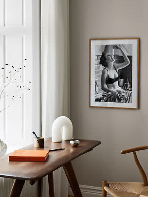 Gerahmtes Schwarzweißfoto an beiger Wand über einem Holztisch am Fenster
