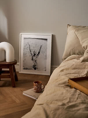 Bedroom with beige bedding, a small stool, and a framed black-and-white photo leaning on the wall