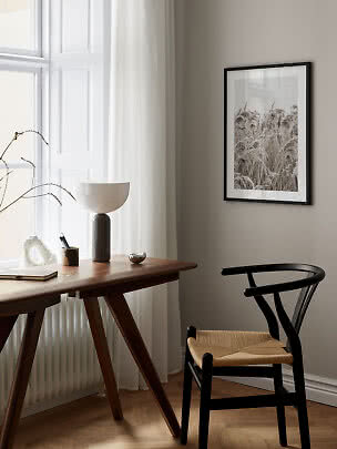 Sort indrammet plakat med siv over et skrivebord i et lyst, minimalistisk rum