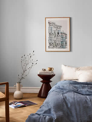 Schlafzimmer mit blauer Bettwäsche und gerahmtem Architekturprint an hellblauer Wand
