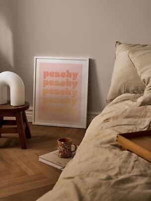 Poster rosa incorniciato 'peachy' accanto al letto con biancheria beige e lampada