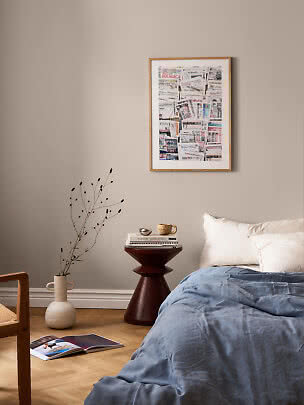 Chambre avec couette bleue, table d’appoint foncée et collage encadré sur mur beige