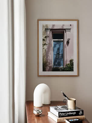 Framed photo of a blue door on a pink facade above a wooden table with books and a vase