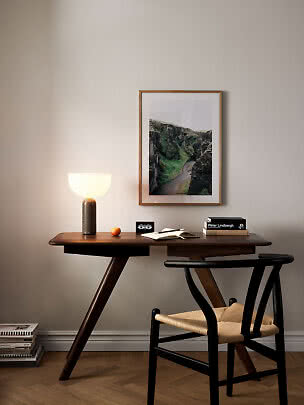 Mørkt træskrivebord med sort stol, tændt bordlampe og indrammet landskabsfoto på væggen