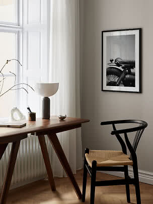 Minimalistyczne miejsce do pracy z drewnianym biurkiem, czarnym krzesłem i oprawioną fotografią motocykla.