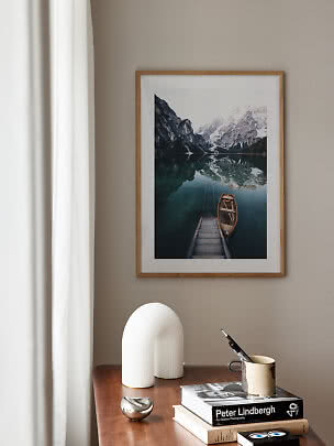 Framed mountain lake print with boat above a wooden table with books and decor