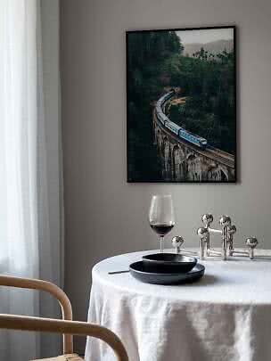 Framed poster of a blue train on a curved viaduct in lush forest above a set dining table