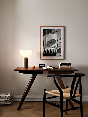 Scrivania in legno scuro con lampada accesa, sedia e poster in bianco e nero incorniciato