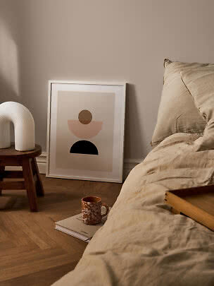 Minimalistisk soveværelse med beige sengetøj, abstrakt plakat, træskammel og hvid lampe.