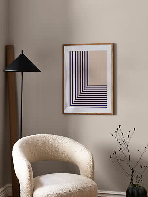 Modern room corner with cream armchair, black floor lamp, and graphic framed print on beige wall.