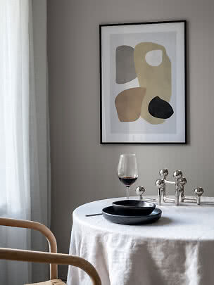 Spisebord med hvid dug, sorte tallerkener, vinglas og sølvstage under abstrakt plakat.