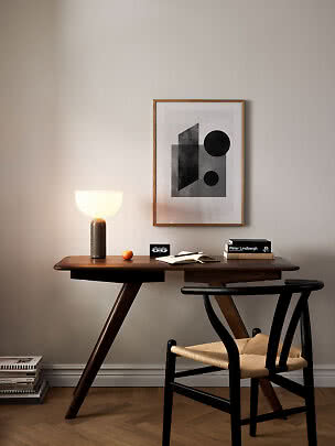 Scrivania in legno scuro con lampada accesa, sedia e quadro astratto alla parete.