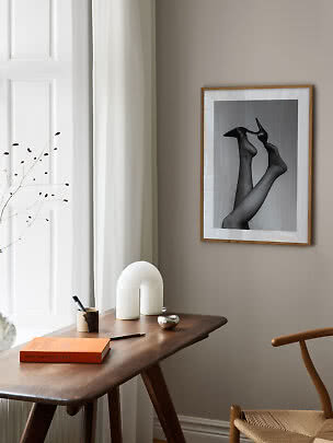 Affiche encadrée en noir et blanc de jambes en talons au-dessus d’un bureau en bois.