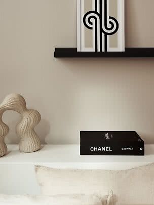 Livre CHANEL noir sur surface blanche avec sculpture beige et art graphique sur étagère.
