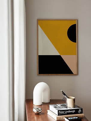 Poster astratto incorniciato con forme geometriche gialle, nere e beige sopra un tavolo in legno