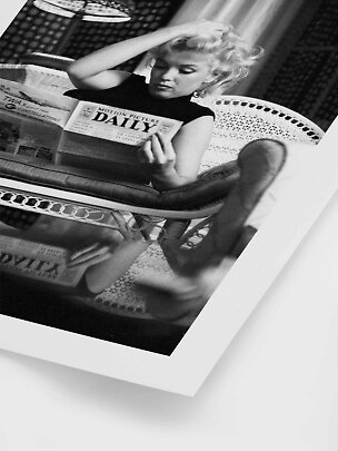 Black-and-white photo of Marilyn Monroe sitting in a chair reading a newspaper