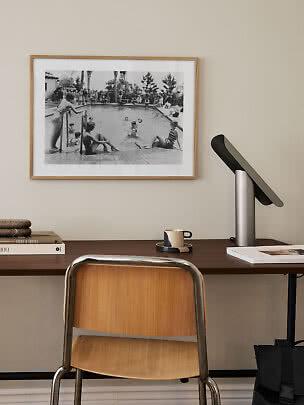 Wooden desk with chair, black table lamp, and framed black-and-white pool photo on the wall