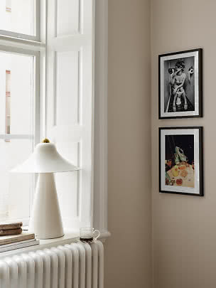Witte tafellamp op vensterbank bij radiator en twee ingelijste posters aan beige muur