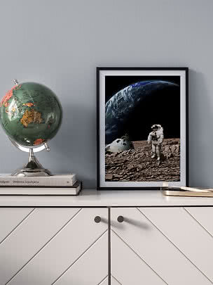 Framed space poster with astronaut on rocky ground and Earth in the background on a sideboard