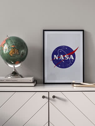 Indrammet NASA-plakat på hvid kommode ved siden af en globus og bøger